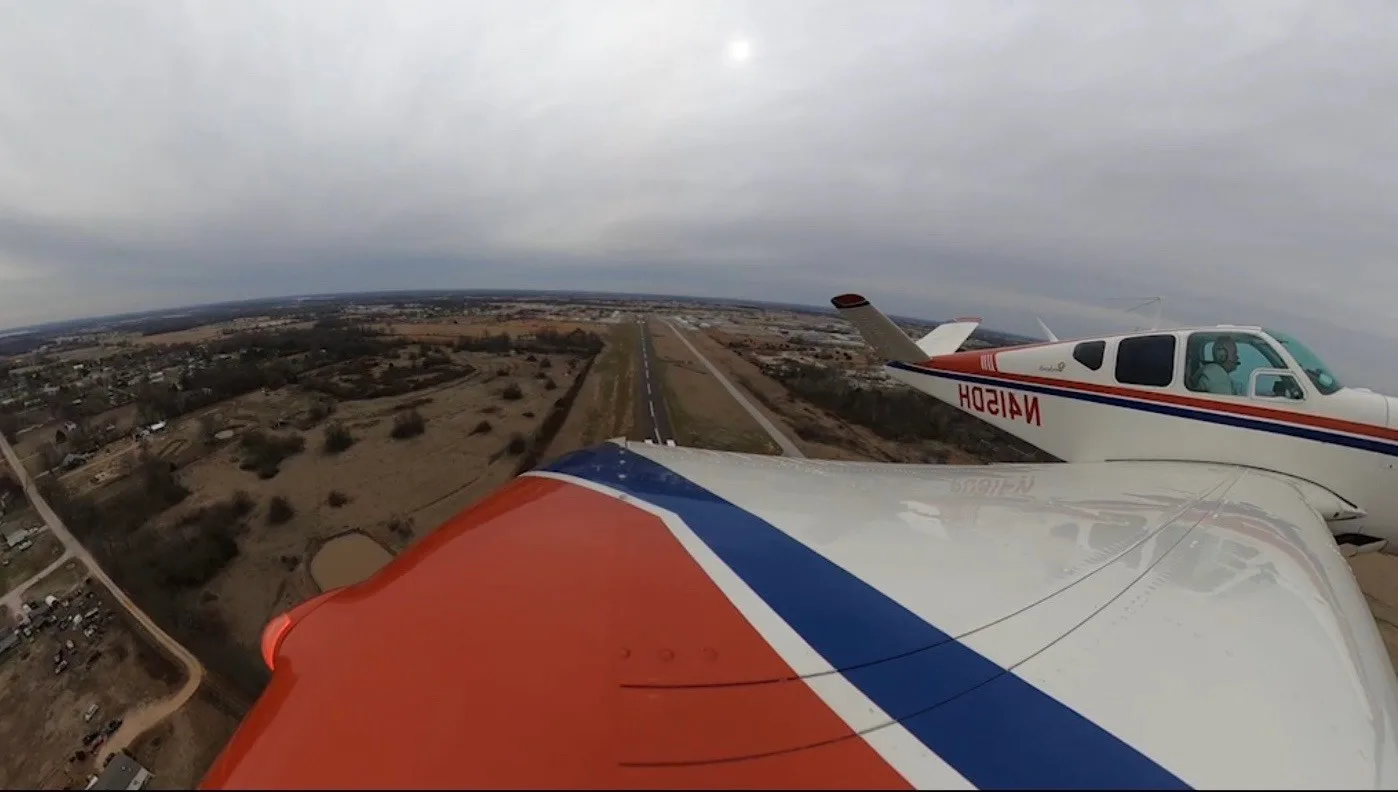 A Beechcraft Bonanza N415DH in flight, seen from the wing, approaching a runway under a cloudy sky.