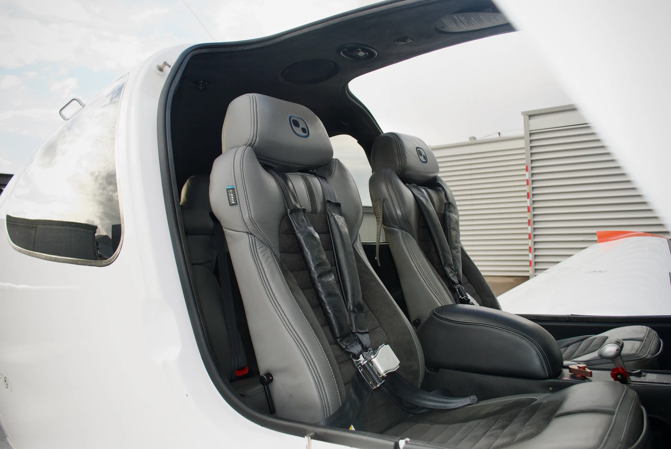 The gray and black leather interior seats of the Cirrus SR22T aircraft, viewed through the open door.
