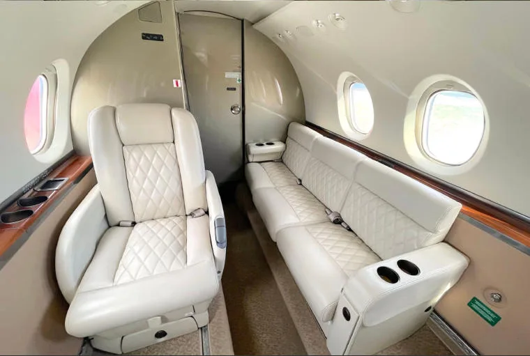 The aircraft's interior cabin showing a single light-colored quilted leather seat and a matching bench seat.