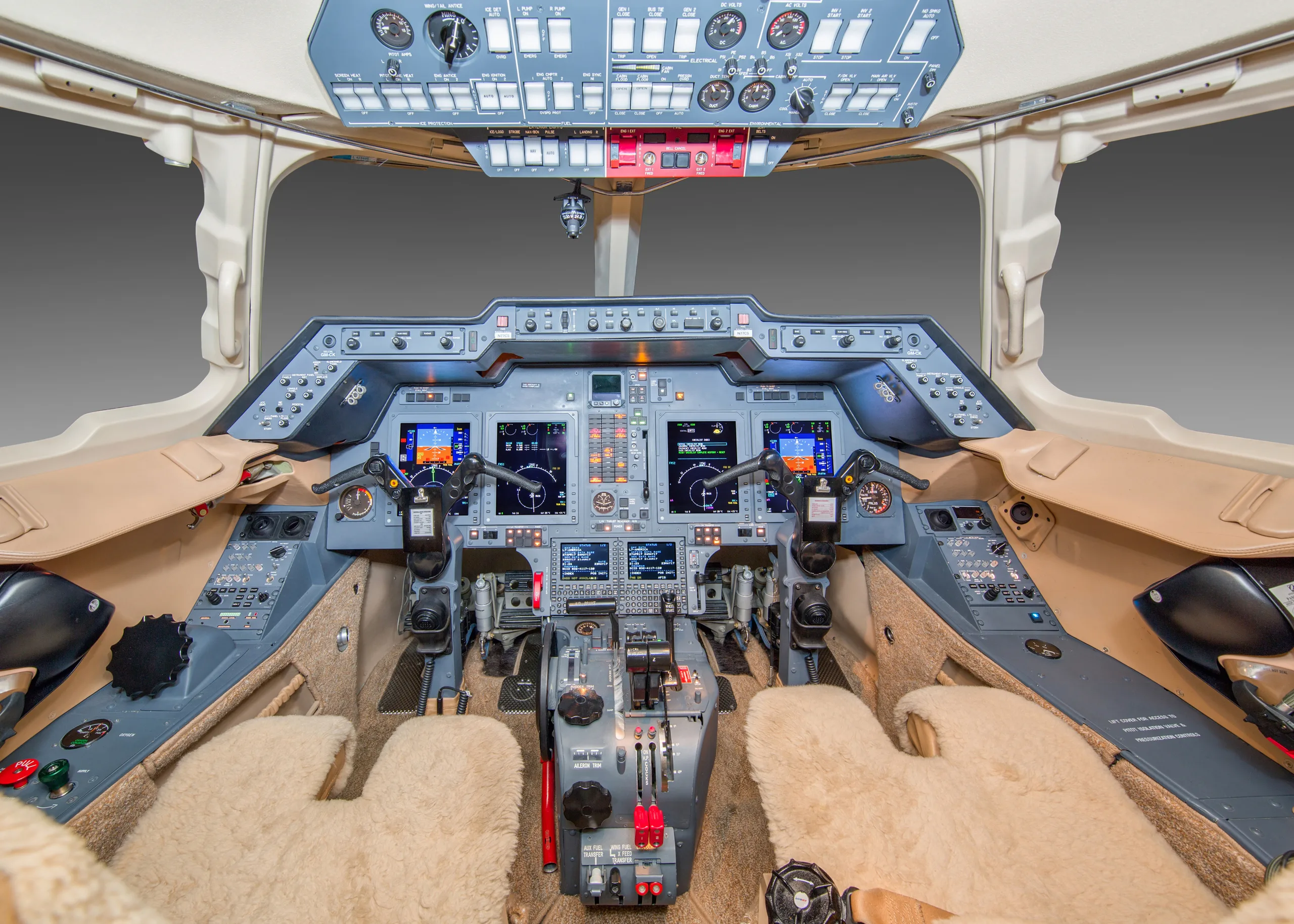 The cockpit of a business jet featuring multiple digital displays, control yokes, and a central throttle quadrant.