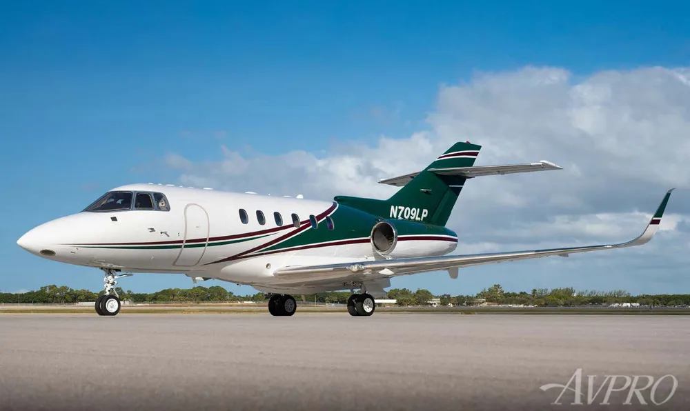 A white and green private jet, N709LP, is parked on an airfield under a blue sky.