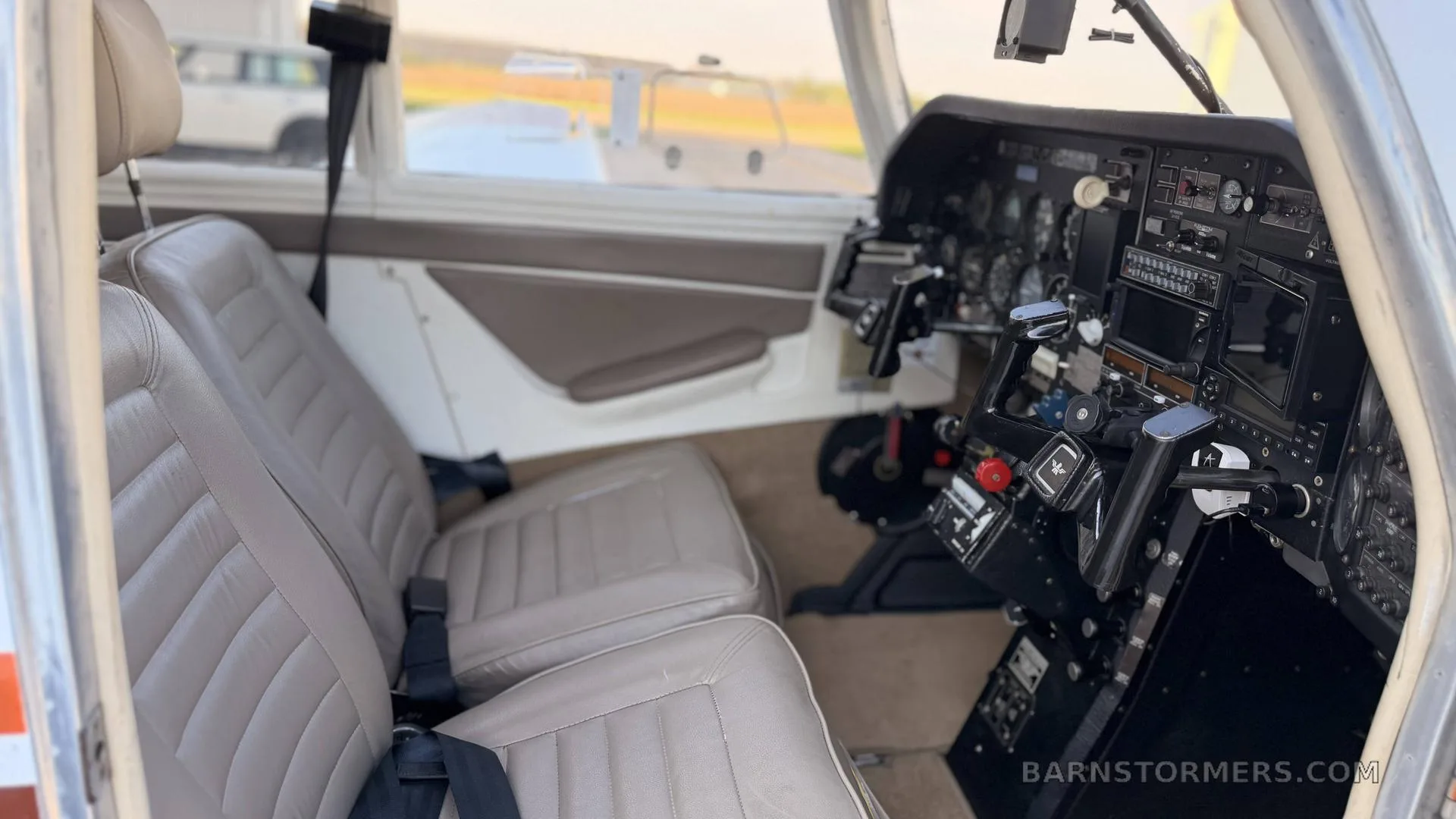The light brown leather interior of a small aircraft, showing two front seats and a partial view of the cockpit.