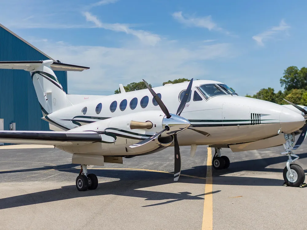 A close-up view of the front right side of a white Beechcraft King Air with dark green and black stripes, showing its propeller and nose.