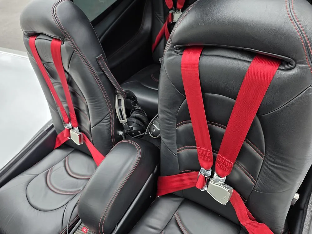 Black leather aircraft seats with red stitching and red seatbelts.