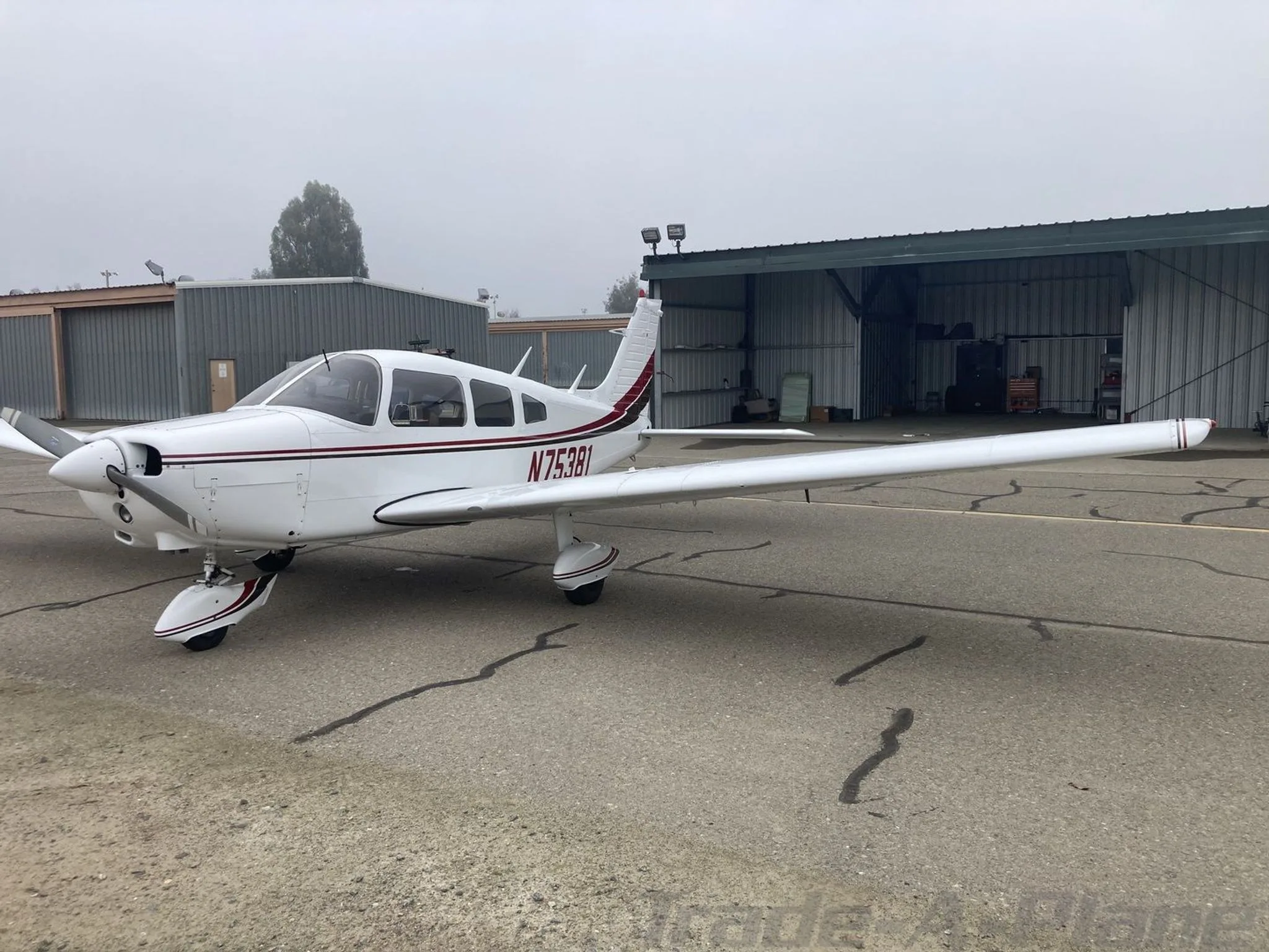 A white Piper PA-28-151 aircraft with red and black stripes parked on an airfield, viewed from the front-right.