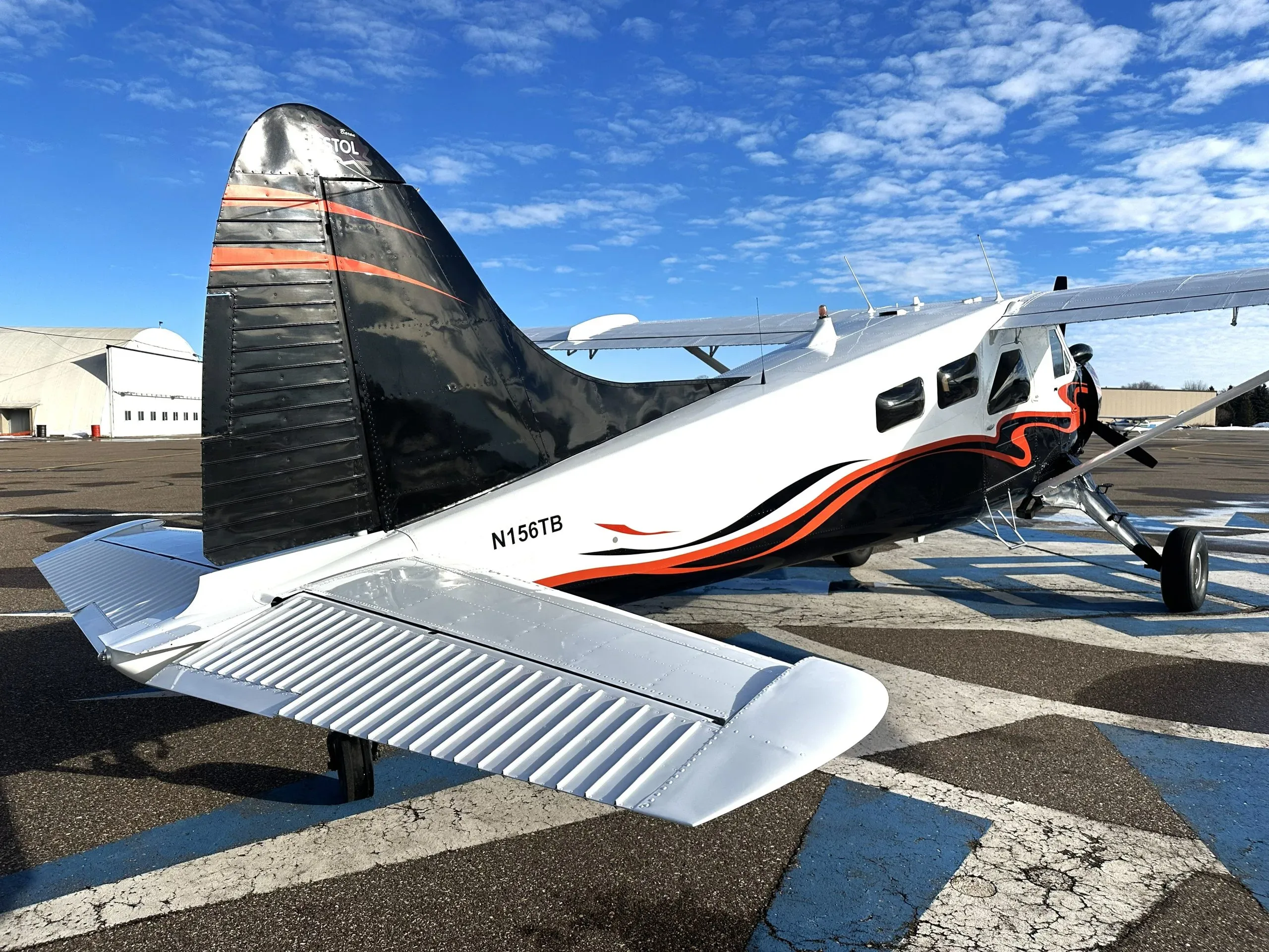 Rear-left view of a white and black single-engine turboprop aircraft with orange accents, showing the tail number N156TB.