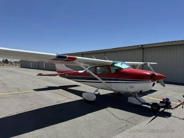 A red, white, and blue single-engine propeller aircraft with a tow bar attached, parked on an asphalt ramp.