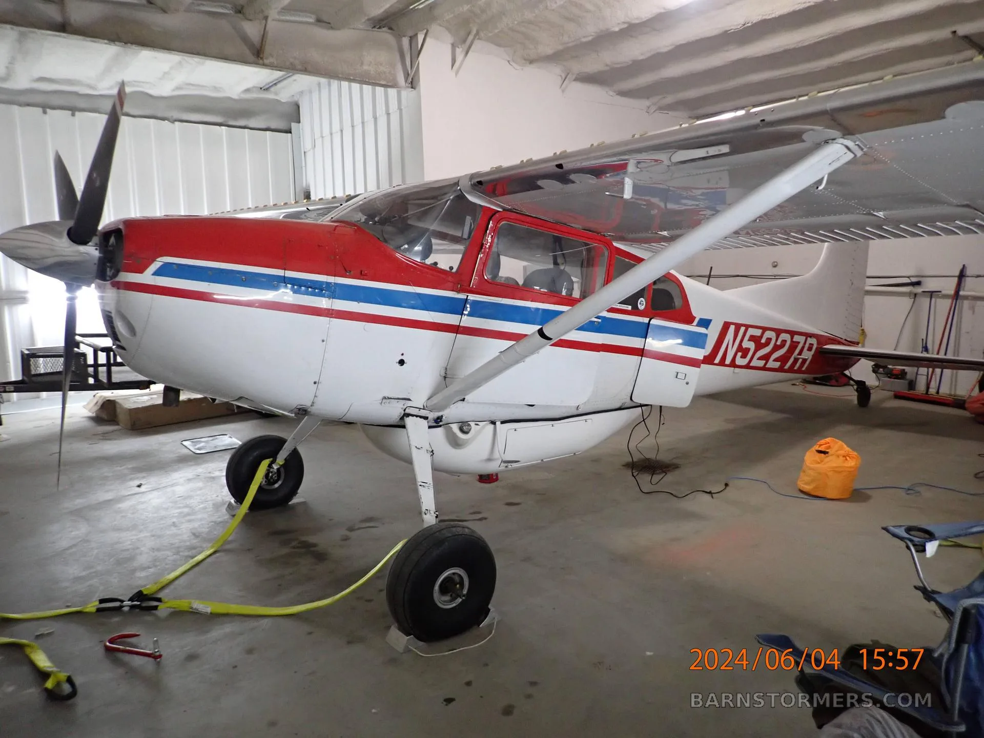 A red, white, and blue Cessna 180 aircraft with registration N5227R parked inside a hangar.