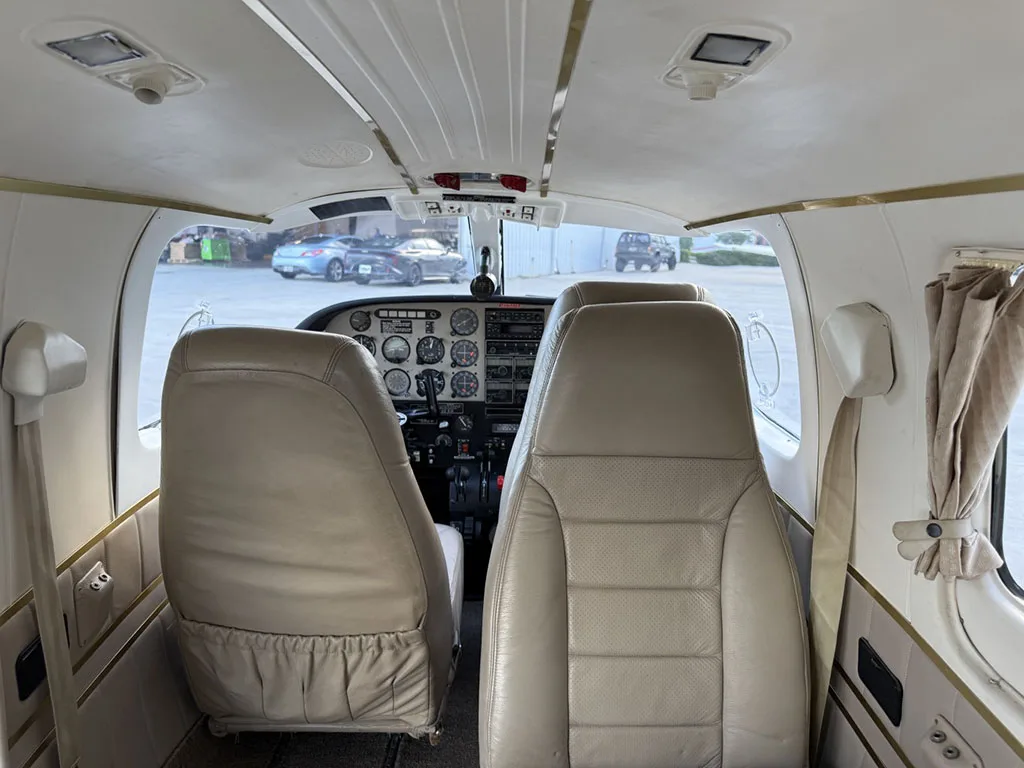 A view from the aircraft cabin looking forward into the cockpit with beige seats and instrument panel visible.