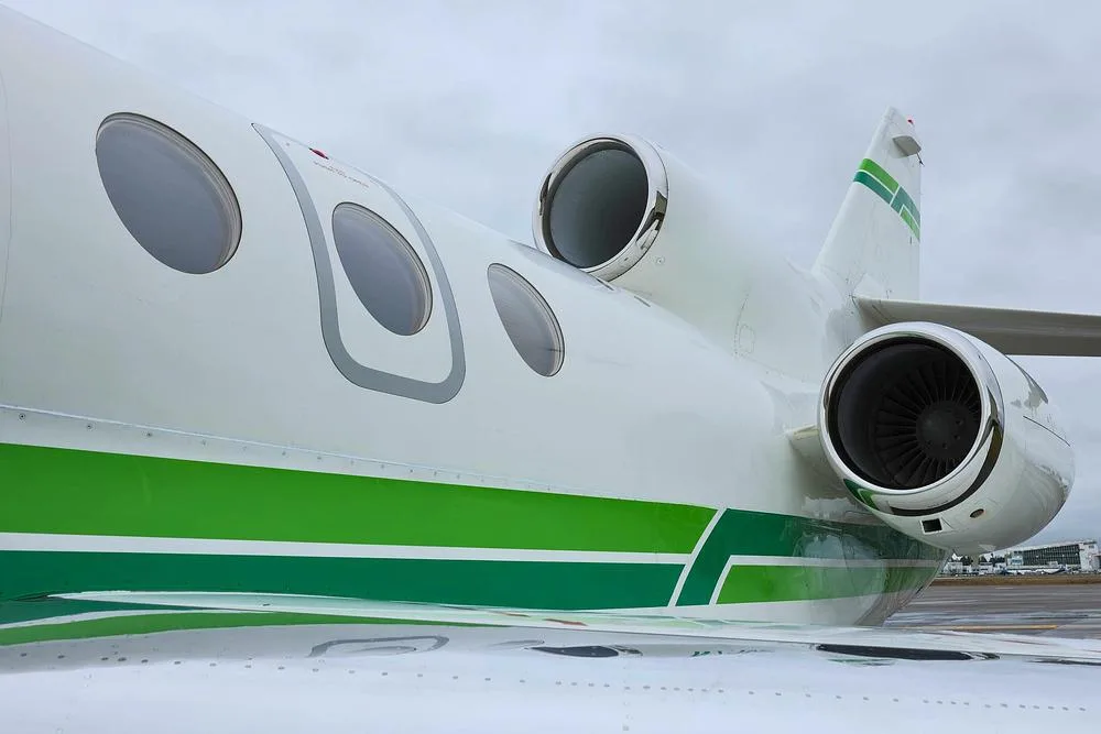 A close-up view of the rear fuselage and engines of a white business jet with green stripes.