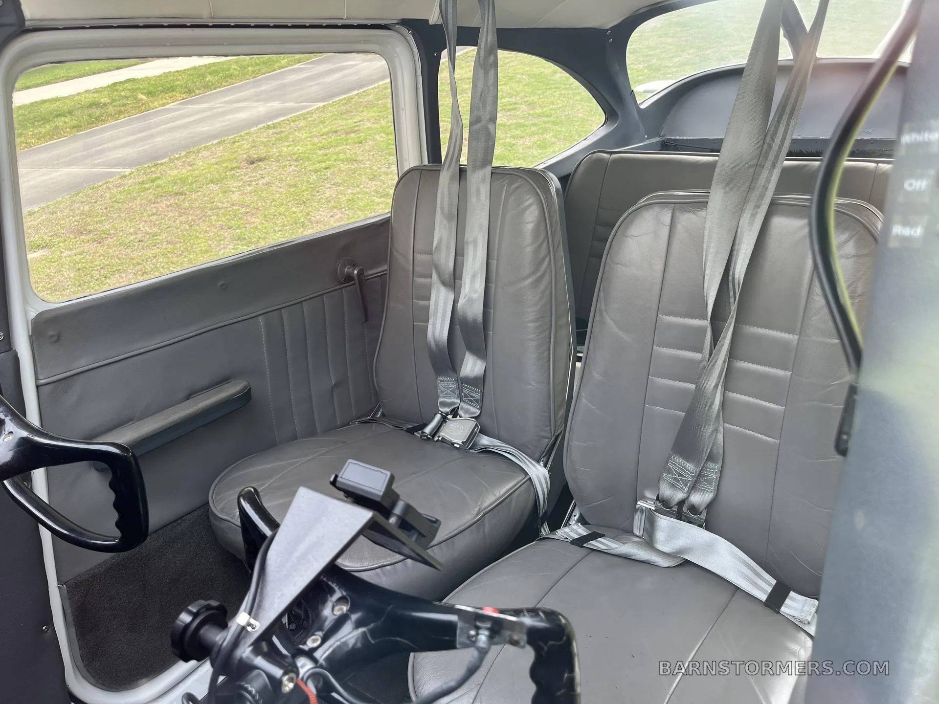 The gray interior cabin of a small aircraft shows two front seats with seatbelts and two rear seats.
