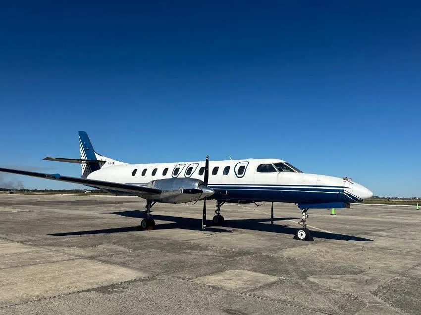 A white and blue Beechcraft 1900 twin-engine turboprop aircraft, registration N-957BA, parked on an airfield under a clear blue sky.