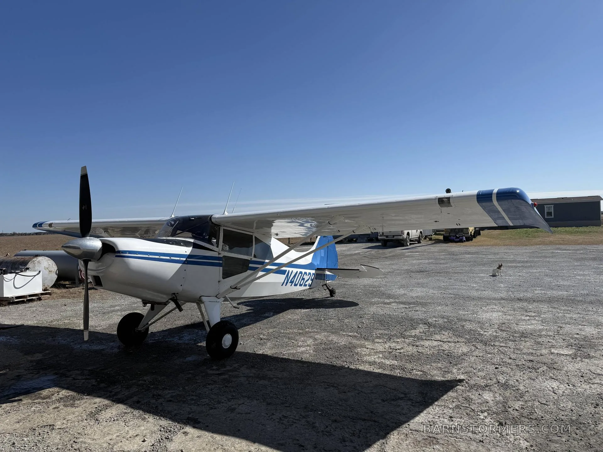 A white and blue Maule aircraft (N40629) with a propeller, parked on a gravel surface, viewed from the front-left.