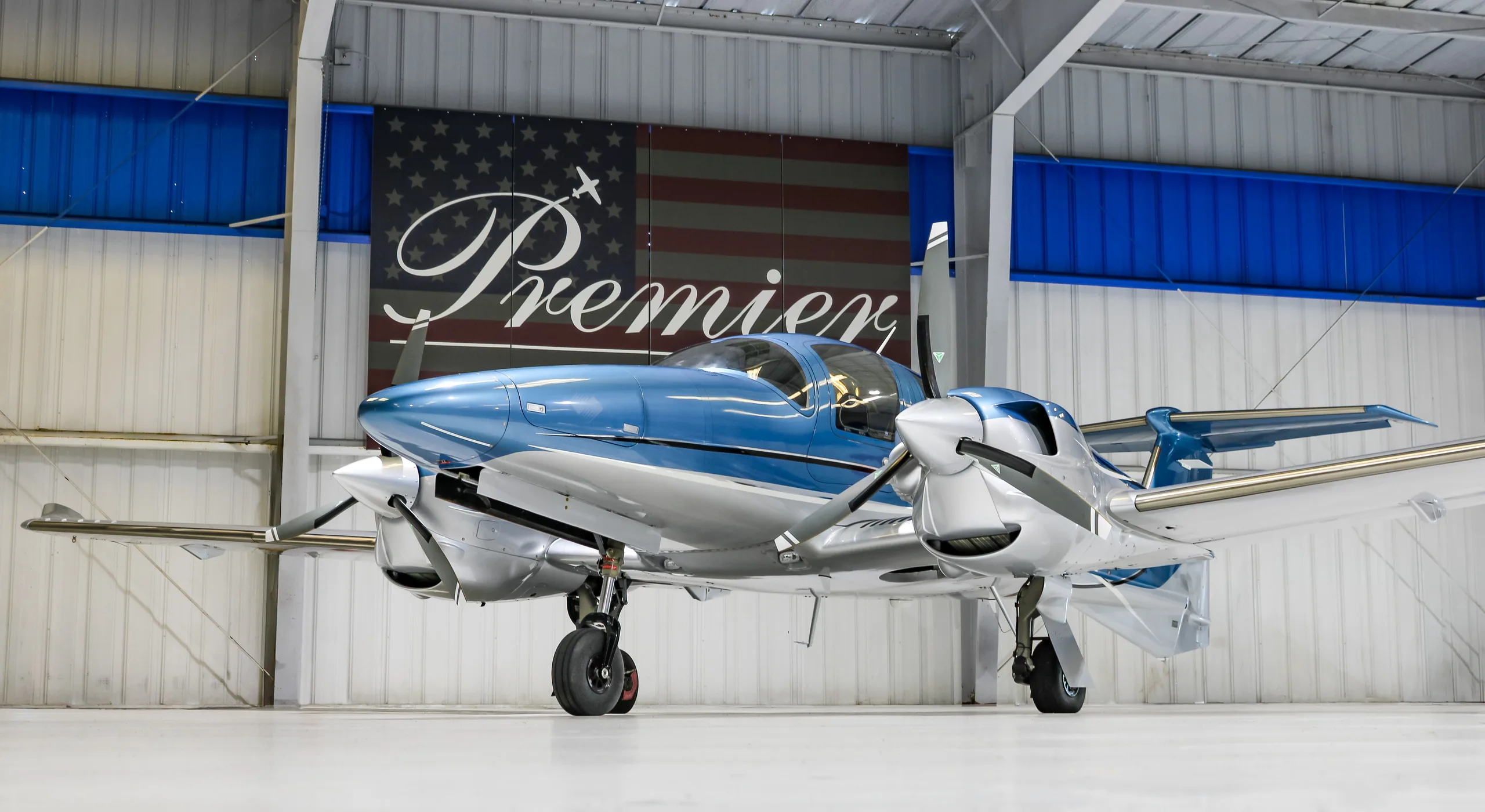 A front-side view of a blue and silver Diamond DA62 aircraft parked in a hangar.