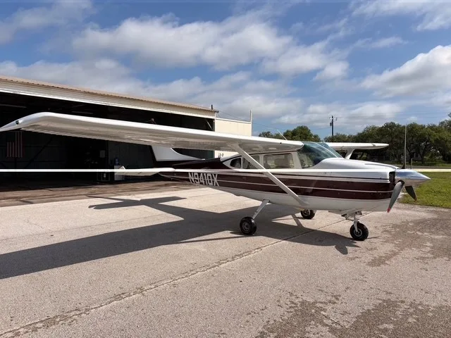 A white and maroon Cessna 182 Skylane (N9410X) parked on an asphalt ramp next to a hangar.