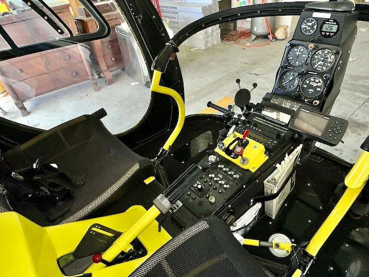 The cockpit interior of the yellow helicopter, showing the instrument panel, controls, and a GPS device.
