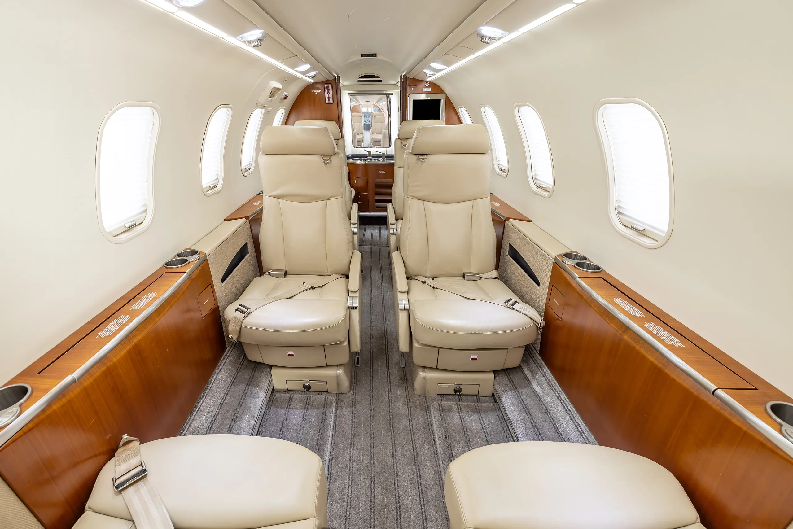 View of the aircraft cabin interior with beige leather seats, wood trim, and a gray carpet.
