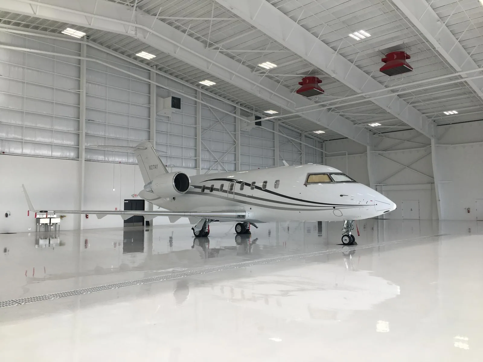 A white business jet with black and grey stripes, tail number N271AY, parked in a brightly lit, spacious hangar.
