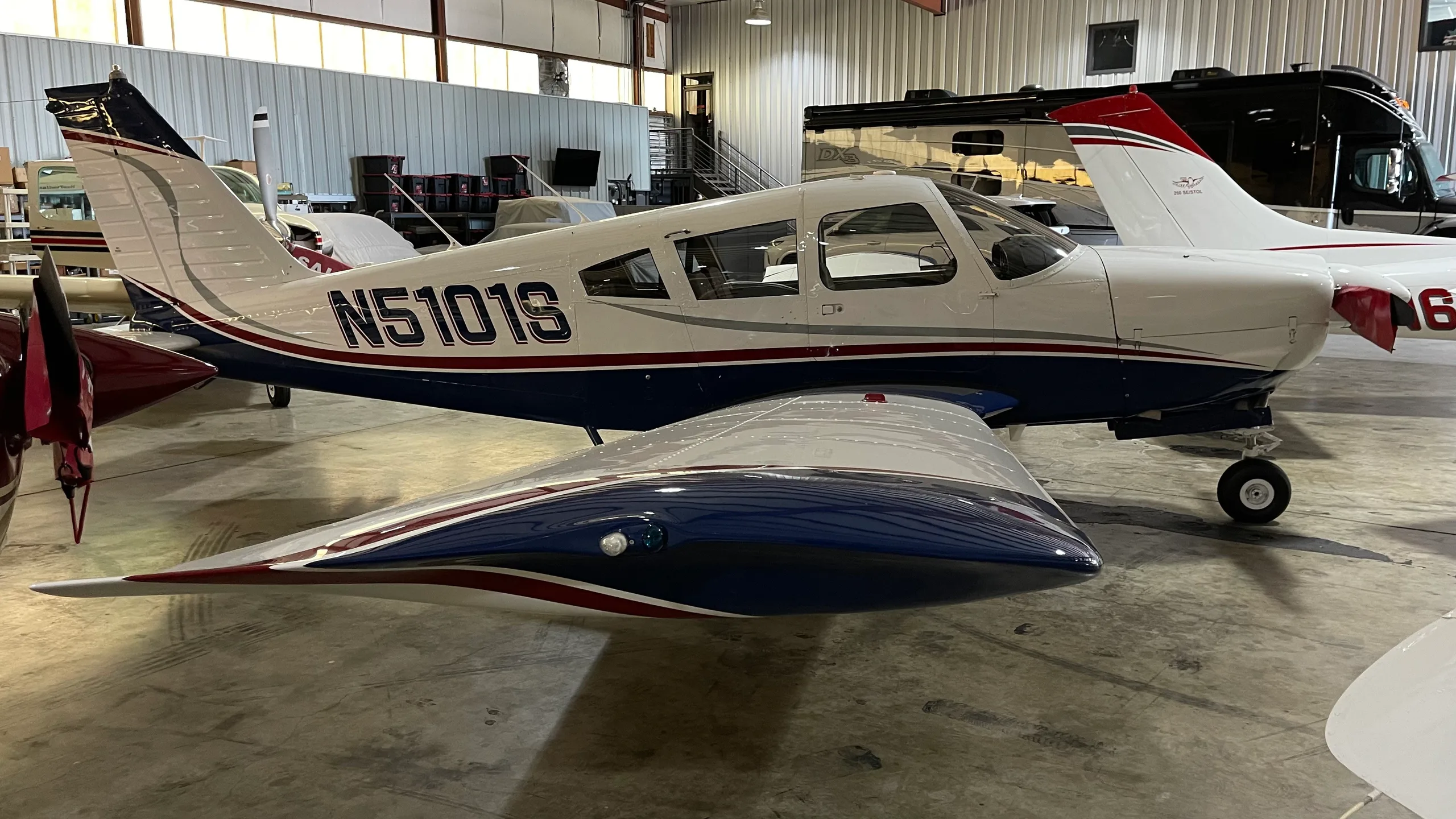 A three-quarter view of the white and blue Piper PA-28-180 Cherokee Challenger (N5101S) parked inside a hangar.