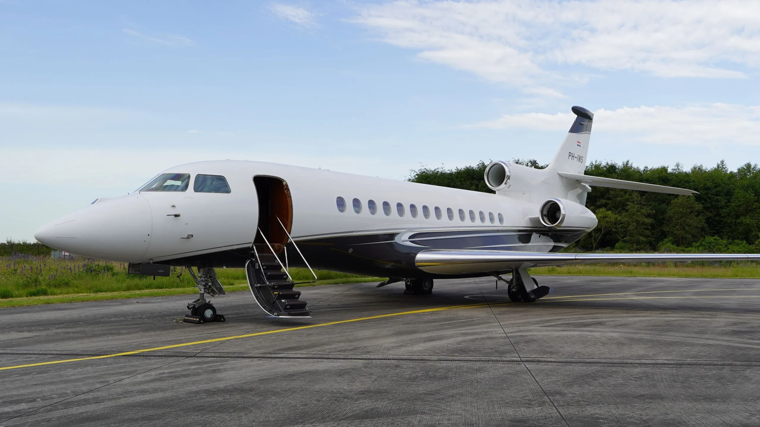 A white and dark blue Dassault Falcon business jet with its main door open and stairs extended, parked on an airfield.