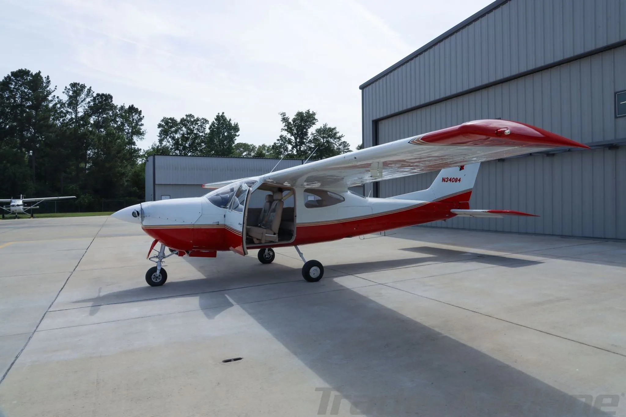A red and white Cessna 177RG Cardinal with its door open, parked on an airfield.