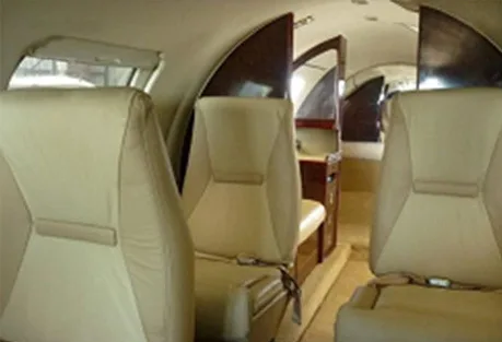 The aircraft's interior cabin features beige leather seats and dark wood paneling.