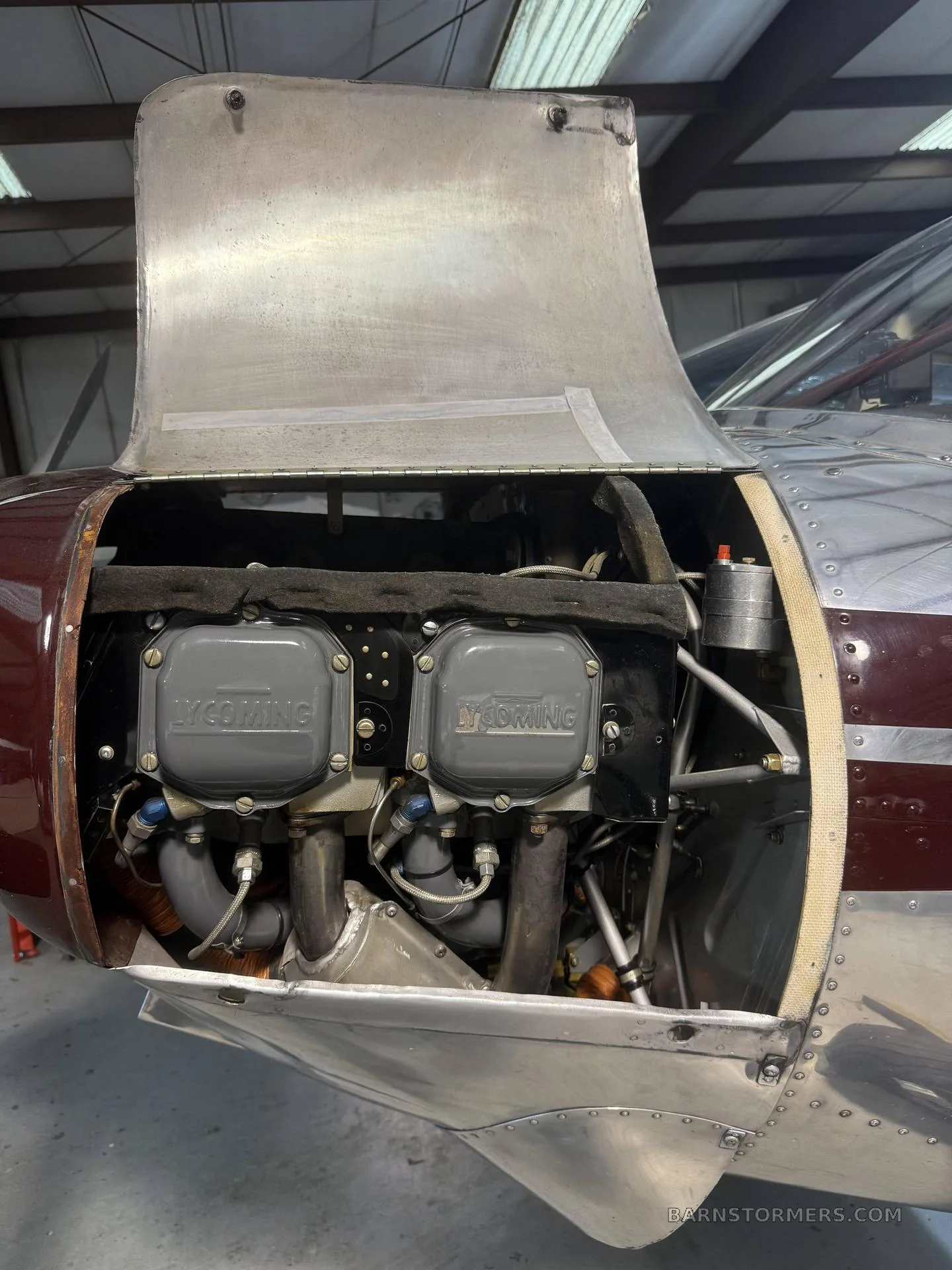 A detailed view of a Lycoming aircraft engine with the cowling lifted, revealing the engine block and exhaust pipes.