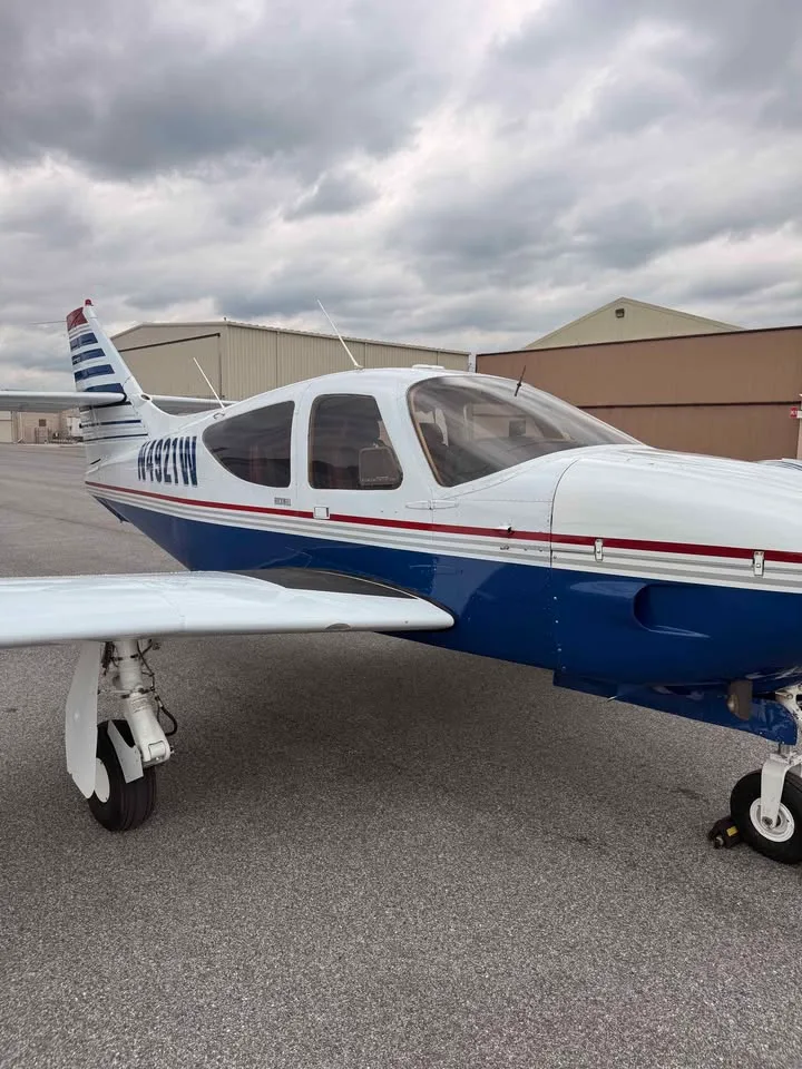 A close-up front-right view of a white and blue single-engine aircraft with registration N4921W parked on the tarmac.