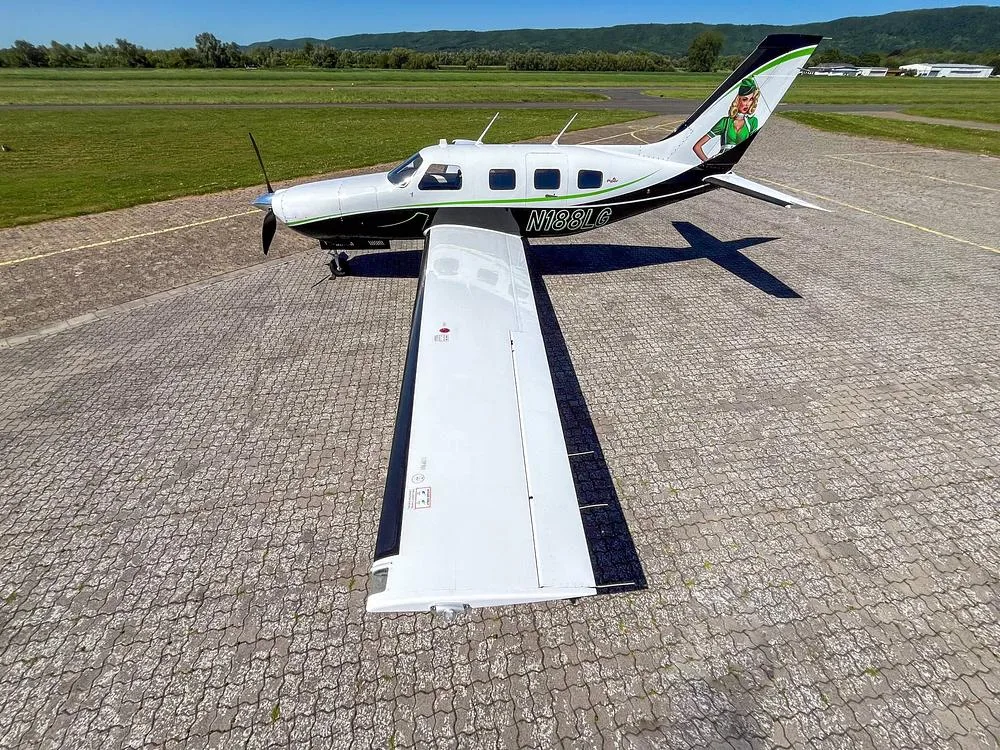 An overhead view of a white and black Piper M-Class aircraft N188LG with green accents and a pin-up girl on the tail, parked on a paved surface.