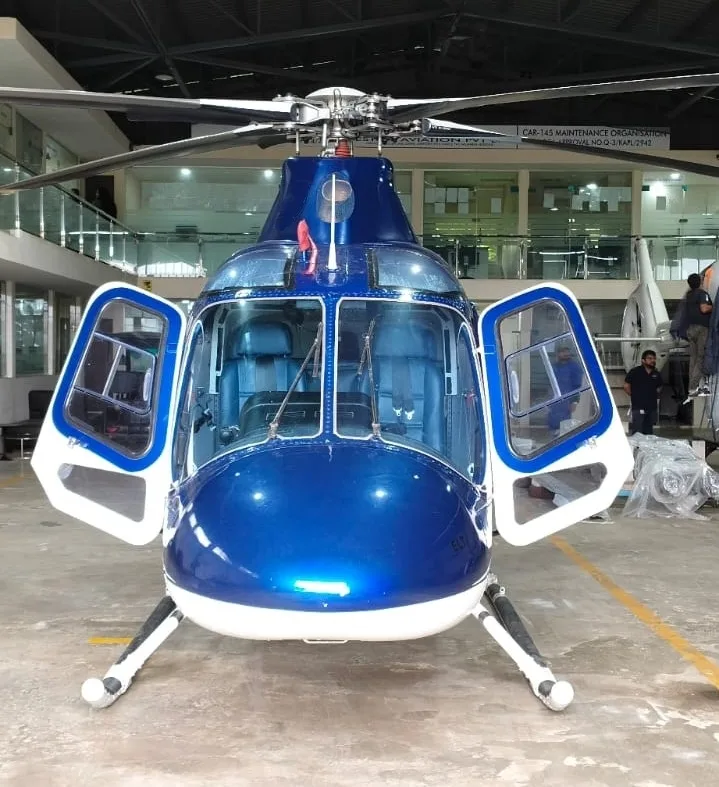 A front view of a blue and white helicopter with its cockpit doors open, revealing blue seats inside.