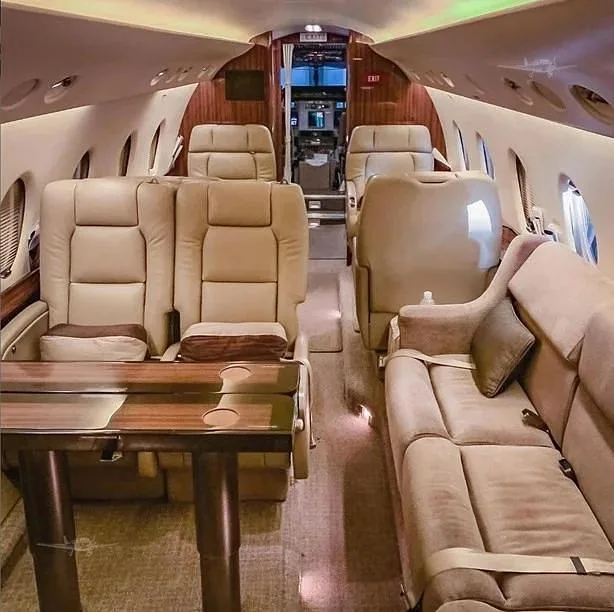 The luxurious cabin interior of a business jet, featuring beige leather seating, a wooden table, and a comfortable sofa.