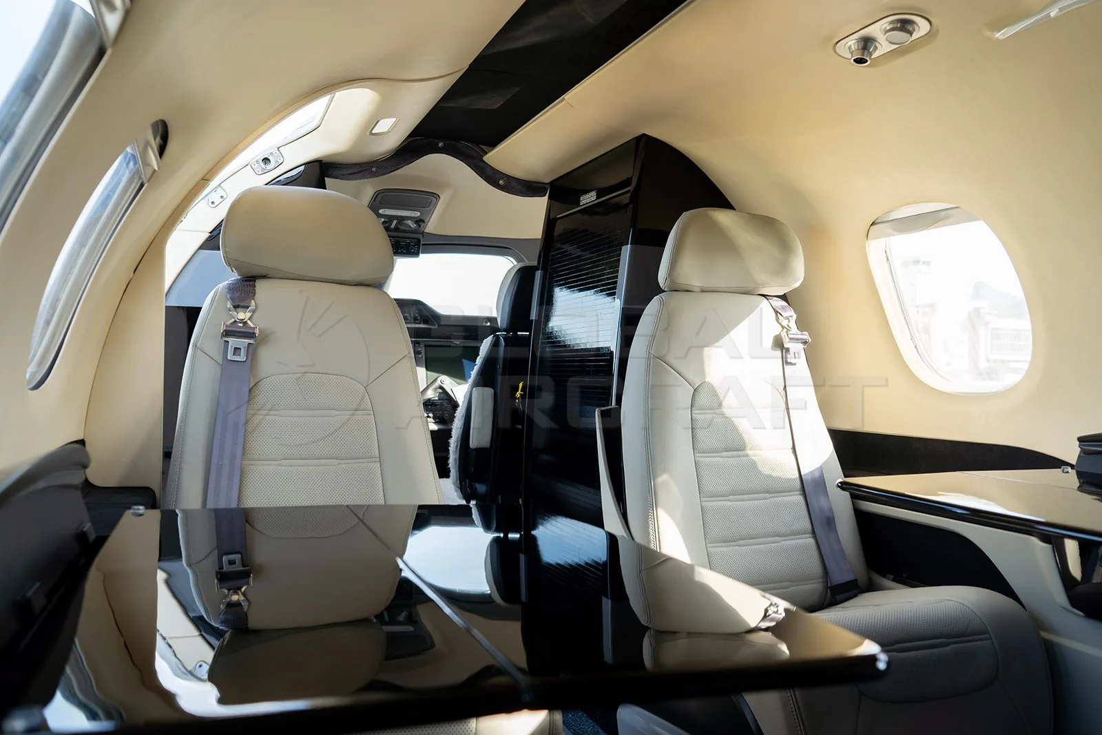The interior cabin of an Embraer Phenom 100 features light beige leather seats and a small table.