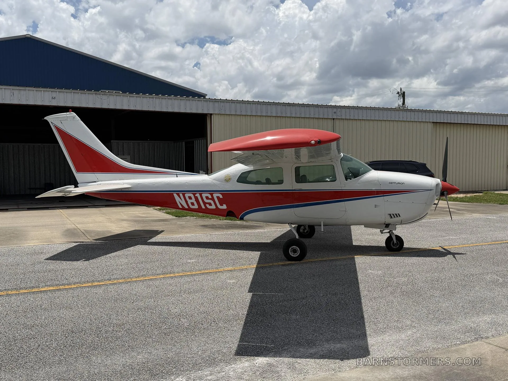 A side view of a white and red Cessna 210 Centurion aircraft, registration N81SC, parked on an asphalt ramp.