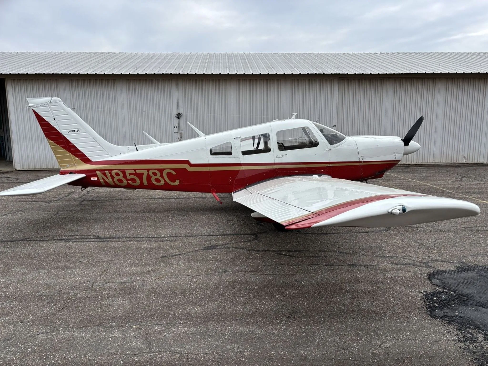 A side view of a white Piper aircraft with red and gold trim, registration N8578C, parked on an airfield.