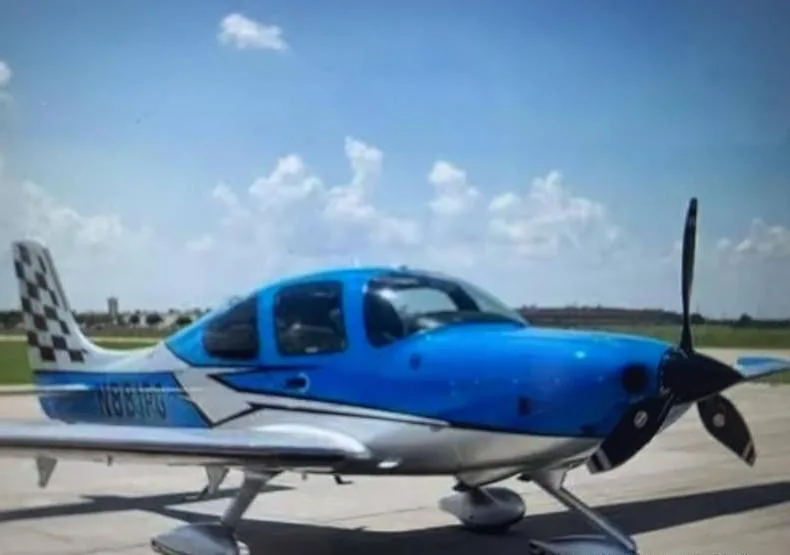 A blue and silver Cirrus SR22 aircraft with a checkered tail, registered N881PG, parked on an airfield under a blue sky.