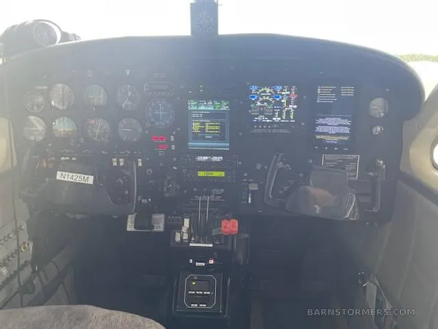 The cockpit instrument panel of an aircraft, featuring analog gauges and modern digital displays, with the registration N1425M visible on the yoke.