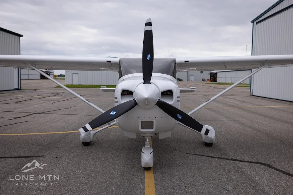 A head-on view of a white Cessna 182 Skylane with a black propeller, parked on an asphalt ramp.