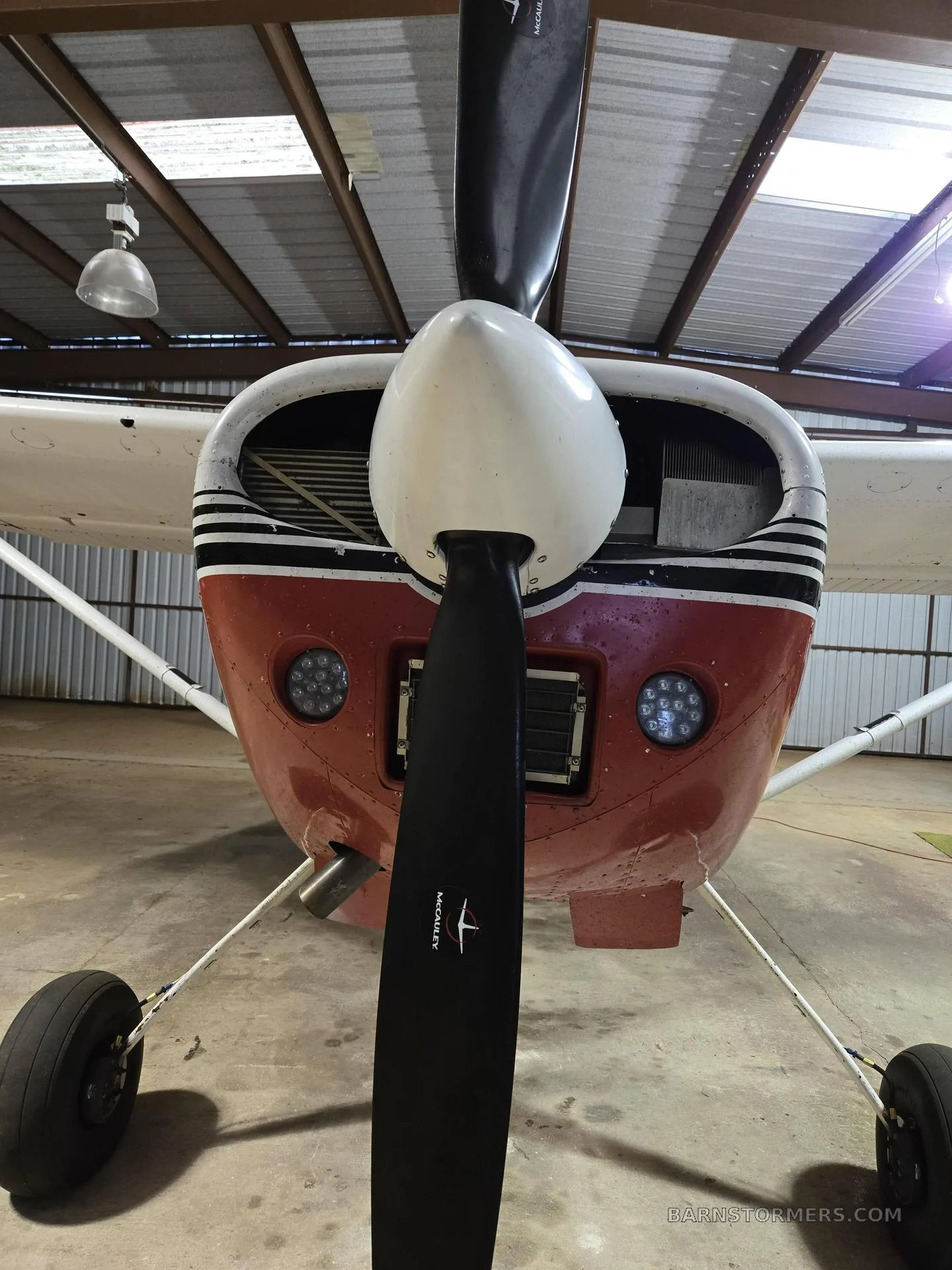 A close-up front view of the red and white single-engine aircraft, showing the propeller and nose cowling.