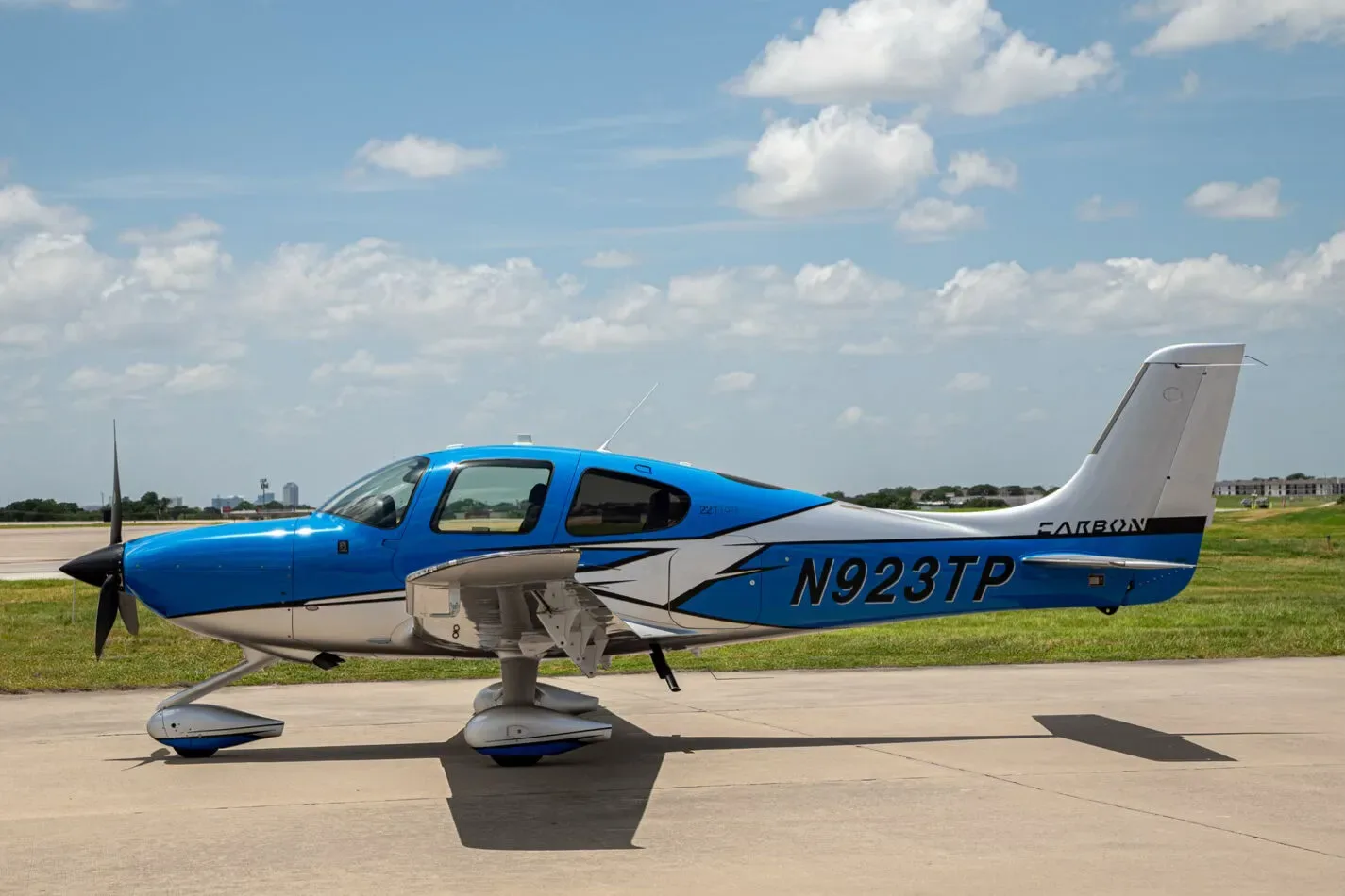 A blue and white Cirrus SR22T aircraft, registration N923TP, parked on an airfield under a partly cloudy sky.