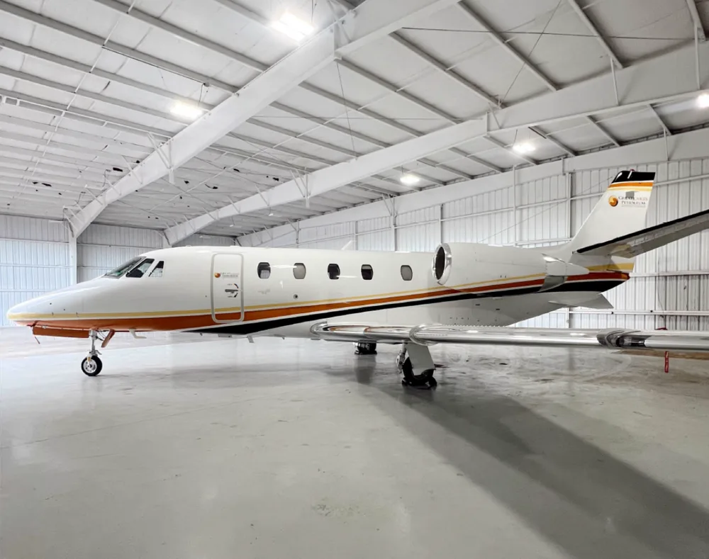 A white business jet with orange and black stripes, parked inside a brightly lit hangar.