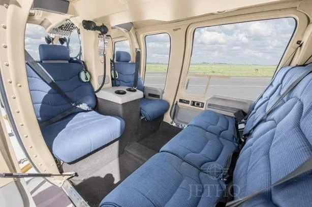 The spacious interior cabin of a helicopter featuring blue quilted seats and a light-colored trim.