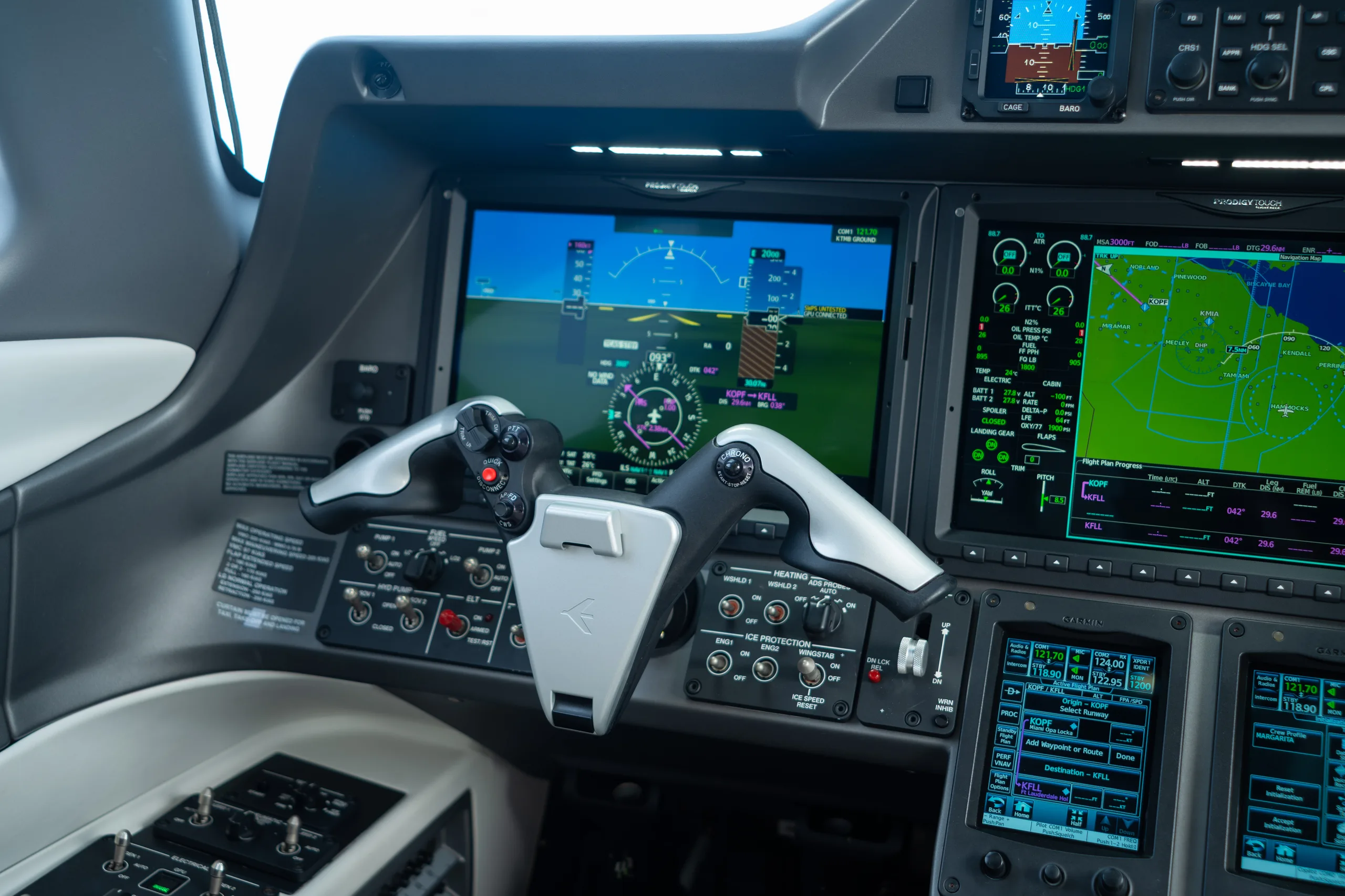 A close-up view of the aircraft cockpit showing the flight controls and multiple digital display screens with flight information.