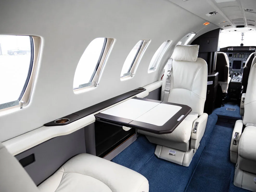 Aircraft interior with white leather seats and a fold-out table, looking towards the cockpit.
