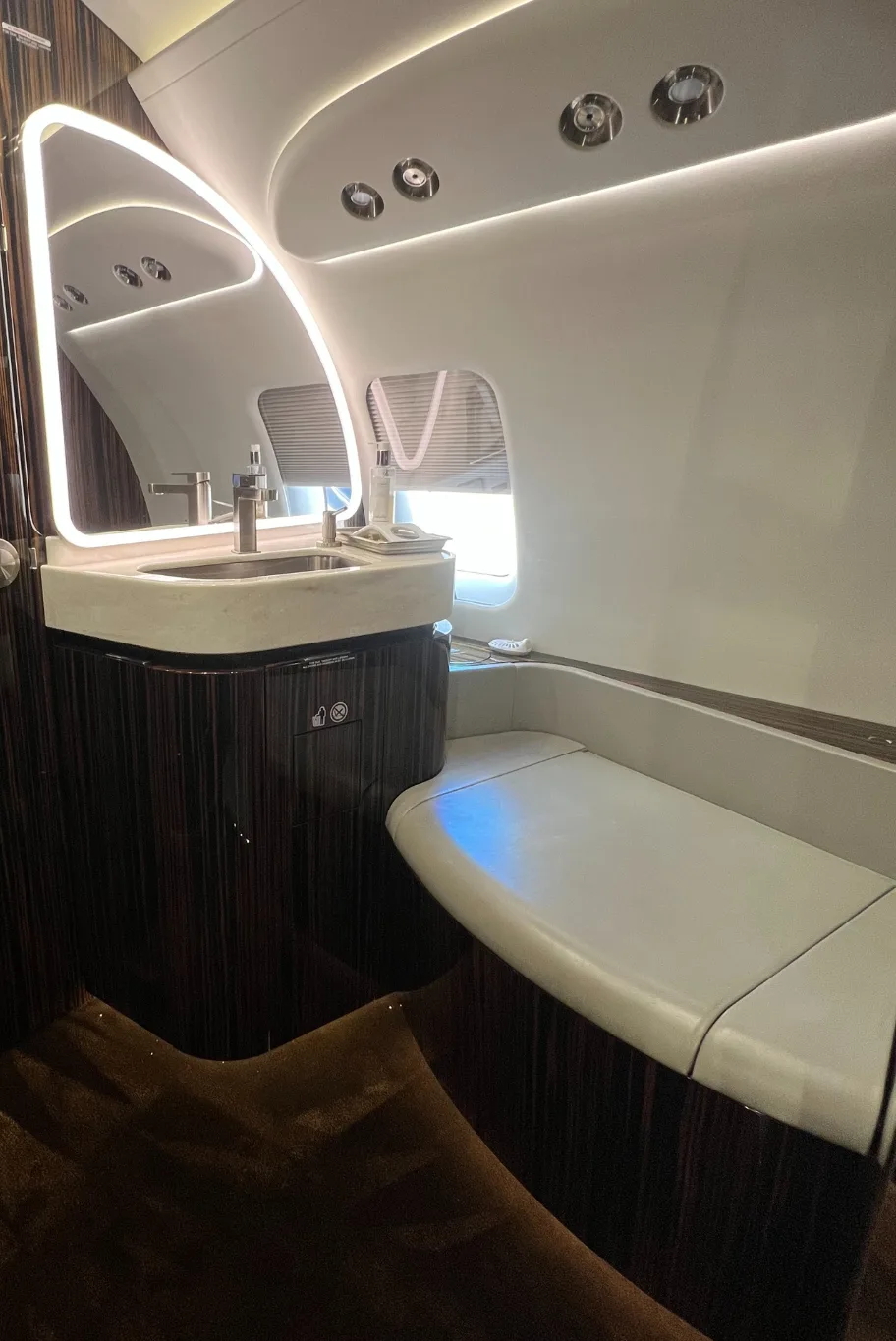 Modern aircraft lavatory with a sink, mirror, and padded bench.