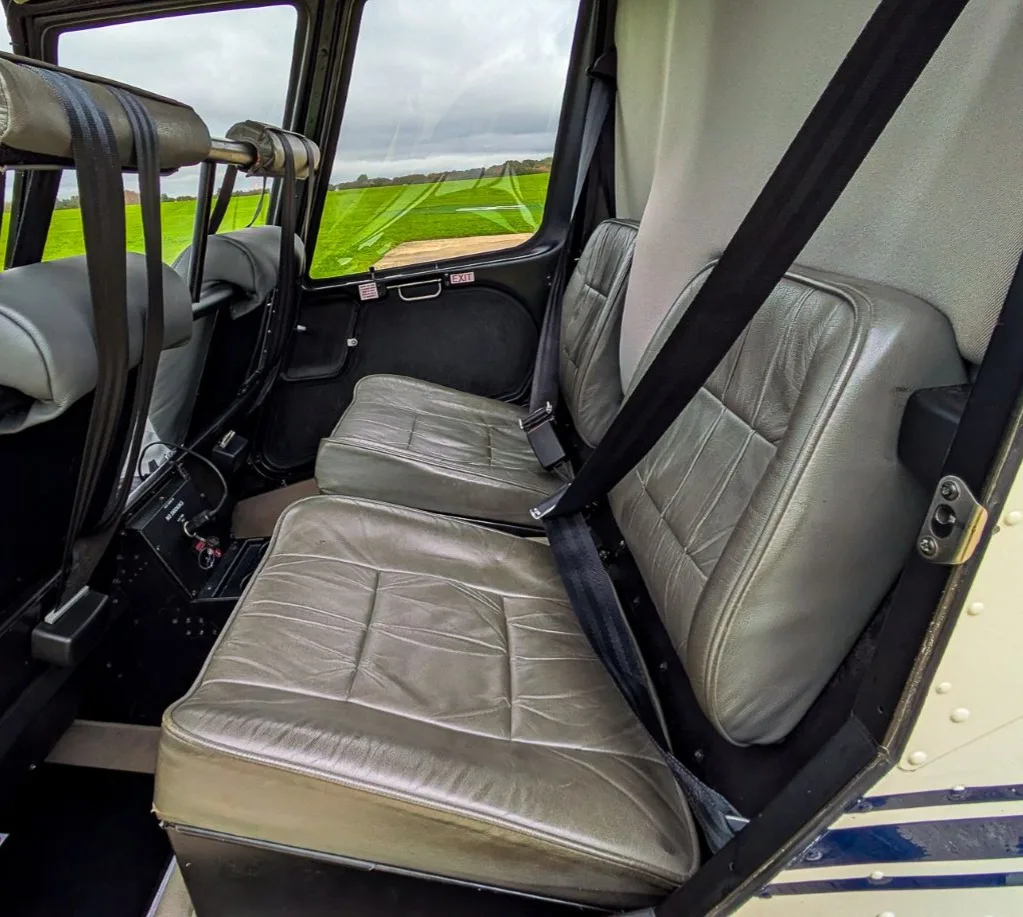 The grey leather rear seats of a helicopter interior, with a view of a green field through the windows.