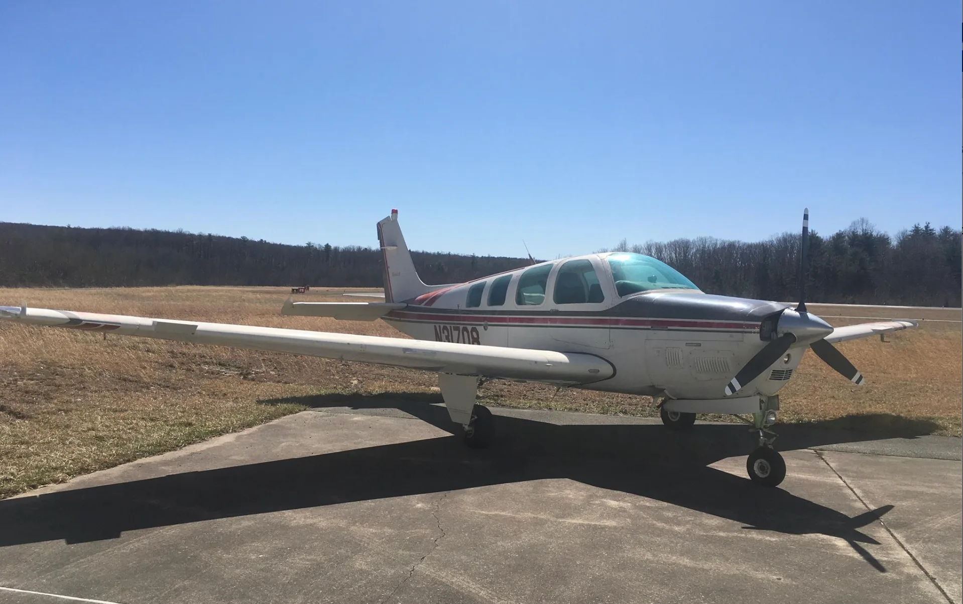 A white and red Beechcraft Bonanza N31708 parked on an asphalt ramp with a grassy field and trees in the background.