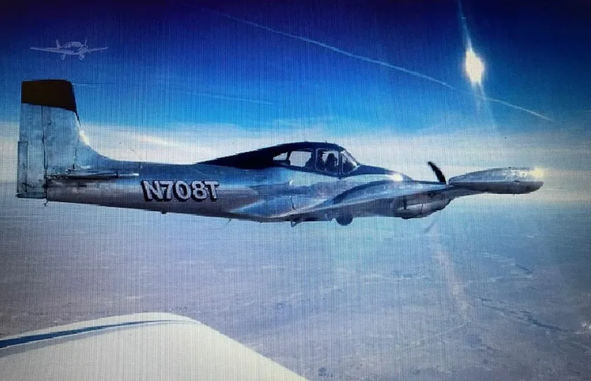 A silver and blue twin-engine aircraft, N708T, flying in a clear blue sky, viewed from another aircraft.