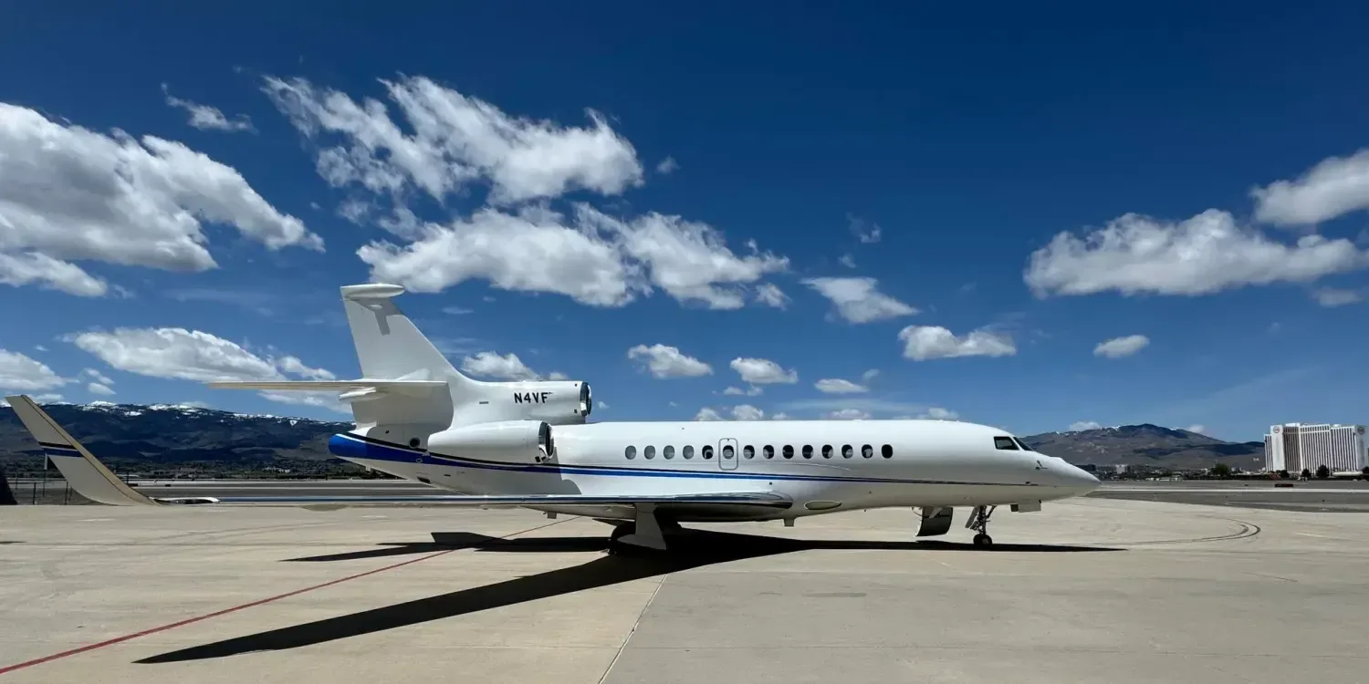 Side view of a Falcon aircraft with a white and blue paint scheme on the tarmac.