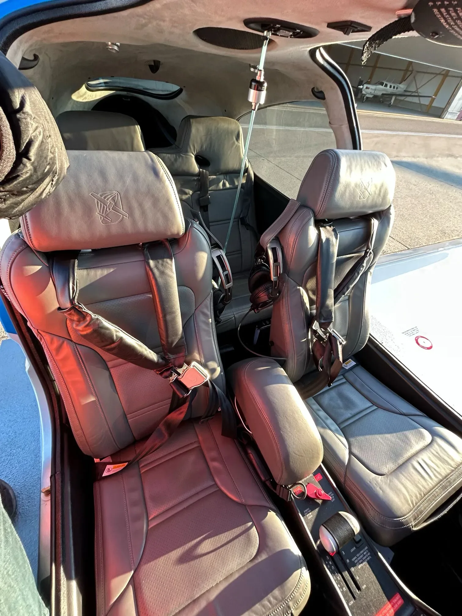 The gray leather front seats of a Cirrus SR22 cabin, showing seatbelts and controls.