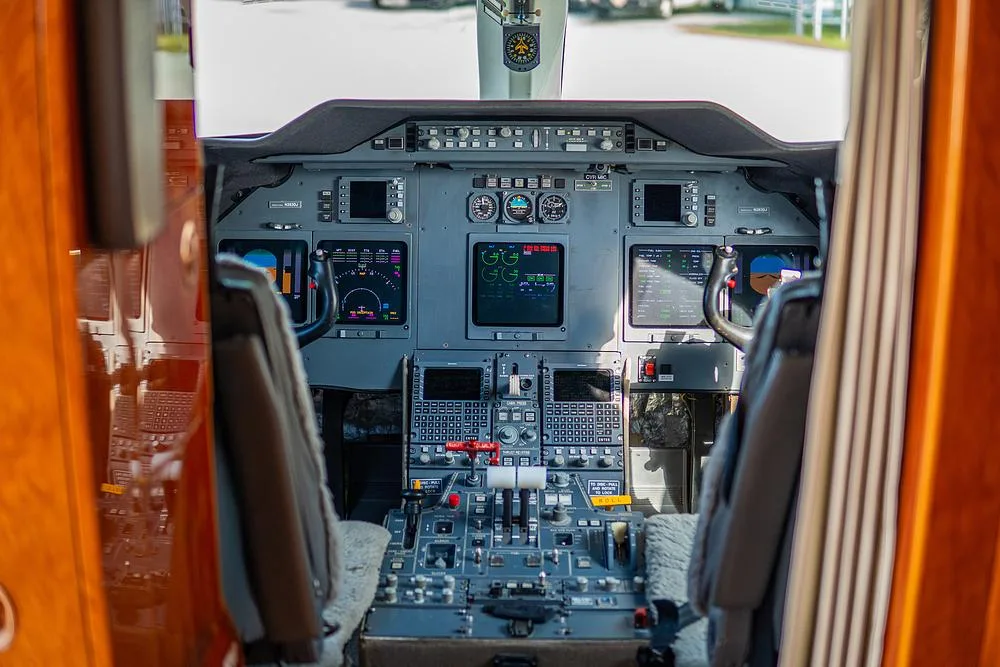 The cockpit of a private jet features multiple digital displays, control panels, and yokes.